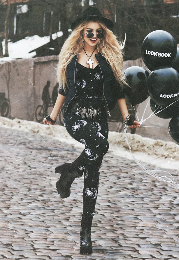 A blonde model holding black balloons, wearing black sun and moon printed leggings and matching top