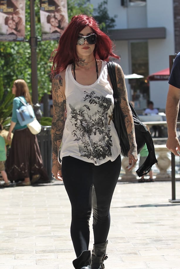 A tattooed woman wearing a graphic printed vest and full-length black leggings and black boots for an alternative inspired style