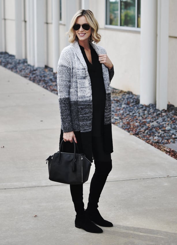 A woman smiles, wearing an oversized cardigan, black full-length leggings and black boots