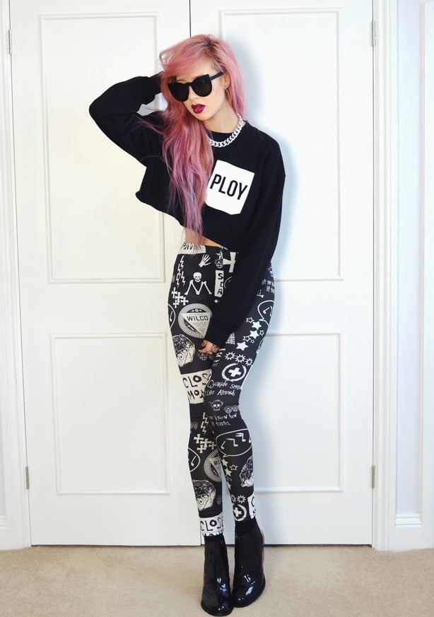 A pink haired woman in sunglasses, wearing a cropped jumper and graphic printed black and white leggings with patent boots