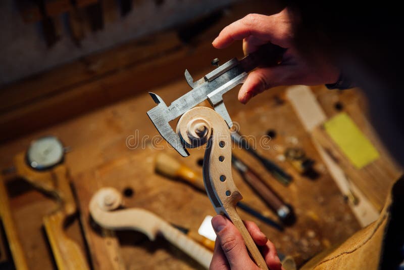 Master artisan luthier working on creation of a violin scroll. detailed work on wood with tools. Men`s hands Measures the thickness of the scroll with meter royalty free stock photos