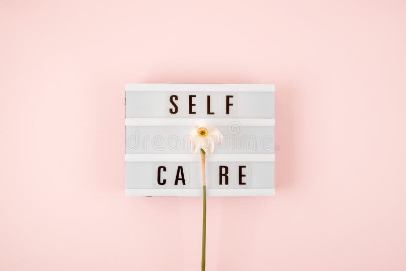 Self-care word on lightbox and flower narcissus on pink background flat lay. Take care of yourself royalty free stock image